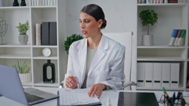 Modern poliklinik ofisindeki internet danışmanlığında konuşan uzaktan kumandalı bir doktor. Kadın doktor videosu hastayı arayıp sağlık verileri yazıyor. Klinikte internetten gülümseyen sıhhiye danışmanı
