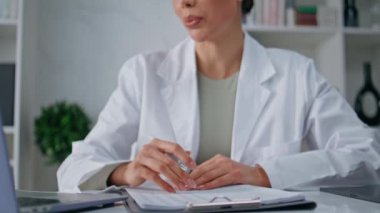 İnternet konferansında dizüstü bilgisayarla konuşan bir tıp uzmanı polikliniğe yakın çekimde hasta bilgilerini not alıyor. Kadın doktor videosu ofiste yazma tedavisini arıyor. Tıbbi çevrimiçi danışma