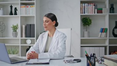 Modern iş yerinde dizüstü bilgisayarlı web kamerası kullanarak klinik uzmanı danışmanlığı. Ofisteki konferansta konuşan beyaz önlüklü profesyonel. Sağlık uzmanının internet sohbeti var.