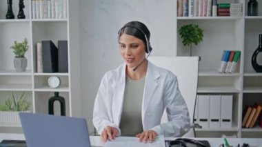 Uzaktan terapist, iş yerinde sağlık desteği sağlayan kulaklıkla çağrıya cevap veriyor. Klinikte kulaklıkla konuşan kadın tıbbi danışman. Doktor tele sağlık hizmeti veriyor..