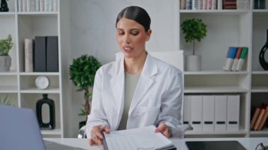 Poliklinik ofisinde dizüstü bilgisayarla yapılan çevrimiçi danışmanlık toplantısı. Ciddi bir kadın doktor sağlık sorunlarını uzaktan tartışıyor. Modern klinikte tıbbi danışman video çağrısı yapıyor.