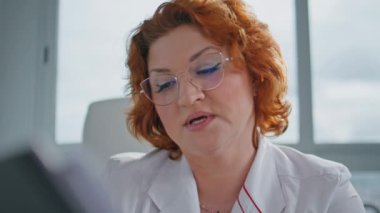 Sağlık hizmeti sağlayıcısı tıbbi muayene kliniğinde belgeleri okuyor. Gözlüklü özenli kızıl saçlı doktor profesyonel konsültasyondaki testlere odaklandı. Hasta bilgilerini inceleyen sağlık görevlileri.