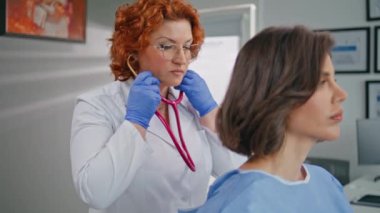 Steteskop kullanan pratisyen hekim klinikte hasta sağlığı kontrolü yapıyor. Beyaz önlüklü kadın doktor dikkatle ziyaretçiyi dinliyor. Sıhhiye, sağlık tesisinde akciğerleri kontrol ediyor.
