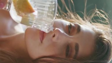 Açık hava güneşli balkonda su içen bir kadın dikey çekimde meyve tadıyor. Romantik kız siestanın tadını yalnız başına çıkarıyor. Güzel model hafta sonu hafif bir rüzgar hissediyor.