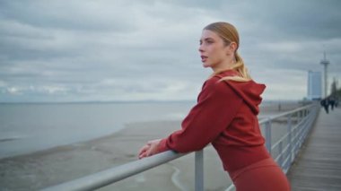Düşünceli kız rıhtımda deniz kıyısına bakıyor. Yakından spor atleti kıyıda dinleniyor spor yaptıktan sonra vücut geriyor. Şehir körfezinde bulutlu okyanusu düşünen dingin, güzel bir kadın. Kentsel yaşam tarzı