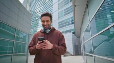 Şehirdeki adam akıllı telefon iletişiminin keyfini çıkarıyor. Modern şehir caddesinde internette sörf yapan gülümseyen İspanyol mesajlaşması. Kulaklığı olan mutlu sakallı erkek dışarıda daktilo eden cep telefonu kullanıyor..