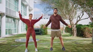 Aktif sporcular sabah antrenman parkında. Odaklanmış erkek kadın şehir bahçesinde ısınma antrenmanına hazırlanıyor. Spor giyim takımında ellerinizi esneterek egzersiz yaparsınız. Sağlıklı kilo verme yaşam tarzı.