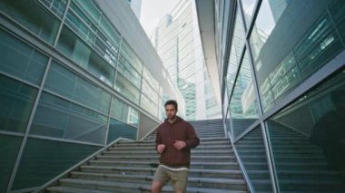 Merdivenlerde koşan atletik bir adam. Yakın plan İspanyol adam modern cam mimarisinde kameraya bakıyor. Şehir merkezini keşfeden yakışıklı bir atlet. Etkin modern yaşam tarzı kavramı