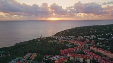 Deniz kenarı manzaralı okyanus manzaralı arka planda inanılmaz altın gün batımı olan bir yer. Deniz alacakaranlıklarında hava manzaralı şehir bölgeleri yeşilliklerle doludur. Akşam ufkunu deniz suyuyla birleştir..