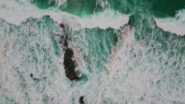 Sahilde köpüren köpüklerle kabaran dalgalar. Bozulmamış akuamarin denizi doğal desenler oluşturuyor. Süper yavaş çekimde kıyıya vuran fırtınalı vahşi su. Deniz manzarası.