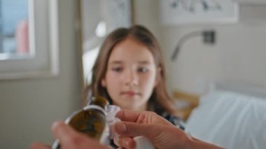 Anne elleri, beyaz yatak odasında hasta bebek için ilaç dolduruyor. Tanımlanamayan anne pijamalarıyla yatakta hasta kızıyla vakit geçiriyor. Anne küçük çocuğa karışımı veriyor. Aile kavramı