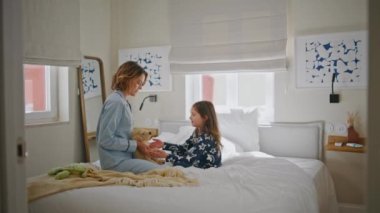 Anne kızı yatakta oyuncak ayıyla oynuyor. Mutlu aile hafta sonu sabahları eğleniyor. Yatak odasının içinde pijamalı, şefkatli bir anne. Çocukluk kavramı