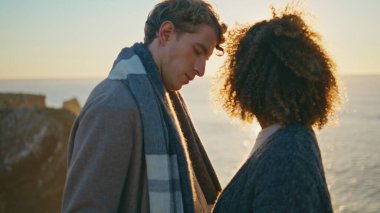 Romantik günbatımı aşıkları yakın çekim. Gençler okyanus sahilinde kucaklaşıyorlar. Deniz kıyısında yan yana duran evli çiftleri rahatlatıyor. Etnik âşıklar, sakin sularda mahremiyetin tadını çıkarırlar. 