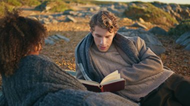 Sakin sakin aşıklar kitap okuyor. Hafta sonunu birlikte geçiriyorlar. Yakın çekim. Güzel, sakin bir kadın akşam doğasında uzanıp romantik pikniğin tadını çıkarıyor. Şefkatli sevgi dolu insanlar okyanus tepesi manzarasında takılıyor.