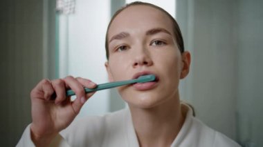 Banyo ortamında diş fırçası kullanan yakın plan kadın. Odaklanmış kız sabah dişlerini fırçalarken kameraya bakıyor. Güzel bir temizlik modeli. Diş sağlığı ve hijyen rutin konsepti.
