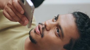 Latin bir adam kafeteryada oturmuş sesli mesaj kaydediyor. Hoparlörden konuşan yakışıklı genç adam dikey çekimde dinleniyor. Bıyıklı serbest çalışan cep telefonu uygulaması ile sesli mesaj gönderiyor