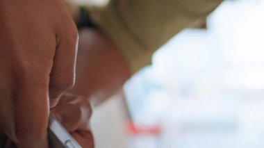 Kafe masasında elinde akıllı telefon tutan bir adam var. Genç Latin Amerikalı adam cep telefonu ekranına bakıyor kahve evi dikey görüntüsünde oturuyor. Sade kafeteryadaki cep telefonunda koyu renk saçlı hipster mesajlaşması.