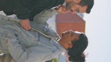 Romantik eşcinsel çift güneşli şehir sokağında durup birbirlerine şefkatle bakıyorlar. Çok ırklı lgbt ortakları kasabada rahatlama hakkında konuşuyorlar. Mutlu homoseksüeller, mutluluğu dikey olarak hissediyorlar..