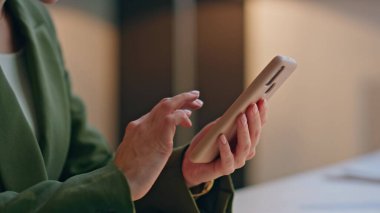 Ofiste akıllı telefon kullanan tanınmamış iş kadını elleri yakın plan. Şirket çalışanı işyerinde internet sayfasında cep telefonu aratıyor. İş kadını parmaklarıyla cep telefonundan fotoğrafları izliyor. 