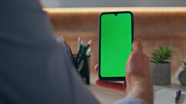 Yakın plan parmak kaydırmalı kromakey ekran cihazı masada. Adamın biri yeşil ekran aletini aşırıyor. Tanımlanamayan iş adamı cep telefonuyla iş yerinde e-postaları kontrol ediyor. İş konsepti