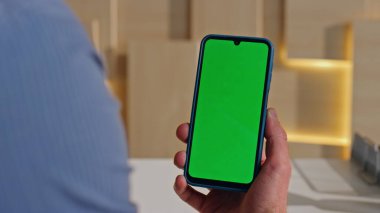 Çağdaş ofisteki Mockup cep telefonundan video izleyen yönetici. Tanımlanamayan iş adamı elinde yeşil ekran akıllı telefonu tutuyor. Şirket yöneticisi krom anahtar telefondaki ortam içeriğine göz atıyor.