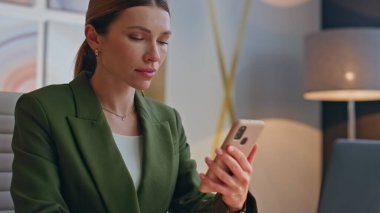 Ofiste cep telefonunu izleyen düşünceli bir kadın. Akıllı telefondan iş e-postalarını okuyan odaklanmış bir iş kadını. Patroniçenin elinde cep telefonu var. Modern odanın içinde Webinar 'ın tadını çıkarıyor.