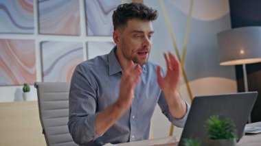 Ajans ofisinde duygusal iş adamı kavgası video görüşmesi. Memnun olmayan patron, iş yerinde dizüstü bilgisayarla buluştuğundan şikayet ediyor. Gergin adam ellerini sallıyor, kızgın hissediyor.