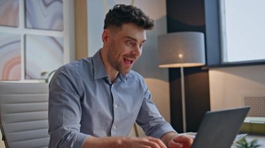 Heyecanlı kazanan iş yerinden memnun, laptopta harika haberler okuyor. Neşeli iş adamı modern ofiste iş başarısını kutlarken mutlu hissediyor. Sevinçten havalara uçmuş girişimci. Sevinç dile getiriyor.