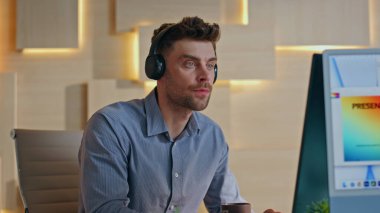 Modern kreatif ofisteki bilgisayarda çalışan kulaklık çizer. Yetenekli genç web tasarımcısı monitörde kablosuz kulaklıkla müzik dinliyor. Rahat yönetici pc ekrana odaklandı