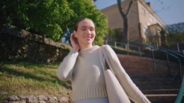 Rahat üniversite öğrencisi güneş ışığı merdivenlerinde tek başına yürüyor. Gülümseyen mutlu kız, bahar parkında çantasıyla gezerken saç stiline dokunuyor. Kaygısız, pozitif kadın mesafeyi arıyor. Rahatlatıcı.