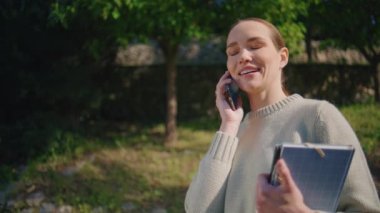 Neşeli bayan hücre paylaşımı hakkında konuşuyor. Sunny Park 'a yakın çekim için iyi haberler. Başarılı sınav sonuçlarına sevinen mutlu öğrenci. Heyecanlı gülümseyen kadın elinde kitaplarla sokakta cep telefonuyla konuşuyor.