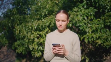Güneşli şehir caddesinde dikilirken akıllı telefon kullanan endişeli kız. Güzel, genç bir bayan cep telefonu ekranında mesaj yazıyor. Düşünceli iş kadını Green Park 'ta e-postaları cevaplıyor.