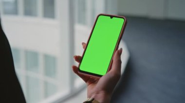 Ofiste el ele tutuşan yeşil akıllı telefon yakın plan. Modern çalışma alanında mobil cihaz. Kromakey cep telefonu kullanan tanınmayan bir kadın yönetici. Model ekrana dokunuyor. Teknoloji ve iletişim konsepti.