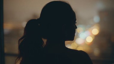 Gece modeli koyu düz arka manzaralı panoramik pencereye bakıyor. Siluet kadın modern lüks evde gelecek planları yapmayı düşünüyor. Esmer kadın gece ışıklarını düşünüyor şehir manzarası yalnız rüya görüyor