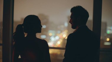 Romantik eşler yıldönümünü kutlayan siluetler şehrin gece ışıkları penceresini kapatıyorlar. Kadın panoramik odasında kadeh kaldırıyor. Güzel aşıklar akşam vakti birlikte eğleniyorlar.