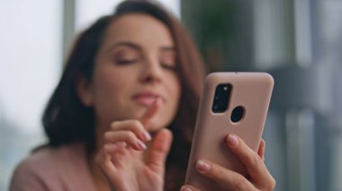 Oturma odasında yakından akıllı telefon izleyen mutlu esmer. Hayalperest kadın mesaj okuyor. Sıcak hafta sonu sabahının tadını çıkarıyor. Gülümseyen model evde cep telefonu tutuyor. Romantik pozitif kız mesajlaşır 