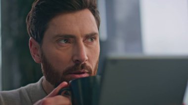 Kapalı mekanda kahve içip tablet mesajı okuyan adam. Sakallı iş adamı elinde bilgisayarla evde cappuccino yudumluyor. Sakin adam serbest dolaşım uygulaması mutfakta tek başına