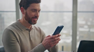 Neşeli adam akıllı telefondan mesaj atıyor. Cam dairede yemek yiyor. Yakın plan. Mutlu gülümseyen adam panoramik dairede cep telefonu mesajlarına cevap veriyor. Pozitif müdür kahvaltıdan zevk alıyor