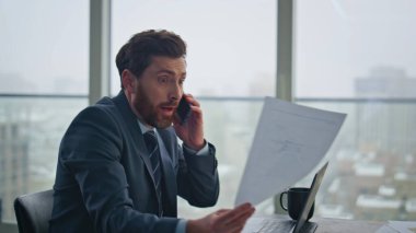 Modern şirket işyerindeki sinirli CEO konuşan cep telefonu tatminsiz iş raporlarını kapatın. Sinirli yönetici lüks bir ofiste gergin bir telefon görüşmesi yapıyor. Kızgın patron içeriyi arıyor.