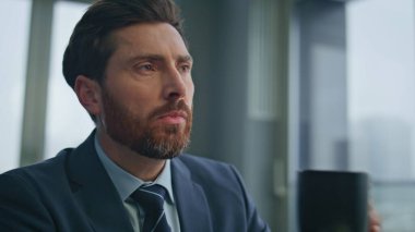 Yakın plan düşünceli patron şehir manzaralı ofiste kahve içiyor. Rahat CEO, çağdaş dolaptaki bilgisayarları kırmanın tadını çıkarıyor. Sakin yönetici tek başına bilgisayarda sohbet ediyor.