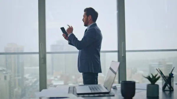 stock image Irritated boss calling smartphone feeling stress at panoramic windows office. Nervous businessman quarrelling at cell conversation. Disgruntled manager ending mobile phone call struggles with emotions