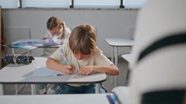 Sınıfta dinleme dersleri alan ciddi bir çocuk. Yakın plan. Düşünceli okul çocuğu elinde kalem tutarak düşünüyor. Akıllı çocuk okul salonunda masa başında oturup öğreniyor. Biraz özenli öğrenci eğitimi.