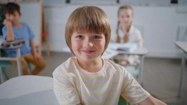 Sınıfta kamera karşısında poz veren gülümseyen çocuk. Küçük mutlu okul çocuğu kabinede yakın plan eğitim veriyor. Küçük çocuk okulda oditoryumda öğreniyor. Sınıf arkadaşlarıyla neşeli bir öğrenci.