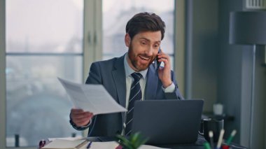 Ofiste evrakları saklayan mutlu profesyonel iletişim hücreleri. Akıllı telefondan konuşan neşeli iş adamı iş anlaşmasının tadını çıkar. Gülümseyen menajer el hareketleriyle tatmin oluyor.
