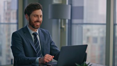 Lüks ofisteki bilgisayarı kullanan mutlu bir adam. Laptop işine odaklanmış gülümseyen bir işadamı. Yakışıklı, sakallı, işyerinde kahve içen bir girişimci. 