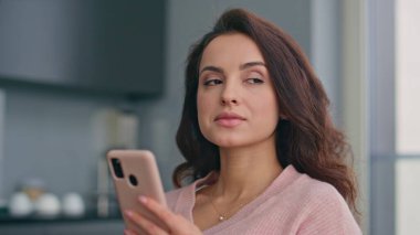 Gülümseyen kadın akıllı telefon ekranına bakıyor ve evde iyi haberlerle mesajları okuyor. Çekici, rahat kız içeride iletişim kurmak için modern telefonu kullanıyor. İnsanların yaşam konseptinde teknoloji 