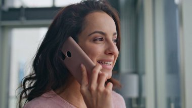 Evde cep telefonuyla konuşan gülümseyen bir kadın. Rahat kız pencereye bakıyor modern dairede eğleniyor. Çekici pozitif kadın hafta sonu akıllı telefon konuşması yapıyor. Tasasız model