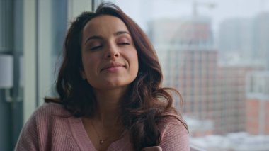 Tasasız model, sabahları yatak odasındaki büyük pencerelere bakarak eğleniyor. Lüks bir dairede rahatlayan kasvetli şehir manzarasını izleyen gülümseyen kadın. Mutlu kız hafta sonları. Güzel bayan hayatı düşünüyor. 