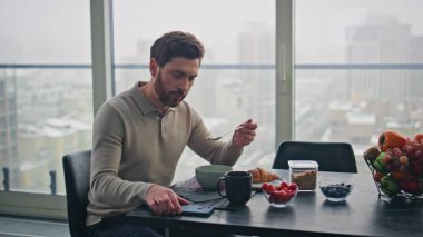 Sakallı adam büyük bir pencerede kahvaltı yapıyor. Yakın plan. Ciddi düşünceli iş adamı panoramik mutfakta endişeli hissederek kötü haber alıyor. Ağız kaplayan üzgün adam düşünme sorunları yaşıyor.