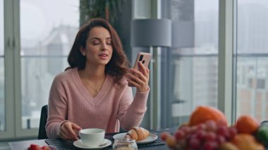 Gülümseyen kız cep telefonuyla konuşuyor panoramik pencerelerde çay fincanı yudumluyor. Güzel esmer kadın elinde cep telefonuyla mutfakta dinleniyor. Kahvesini yudumlayan mutlu bayan...